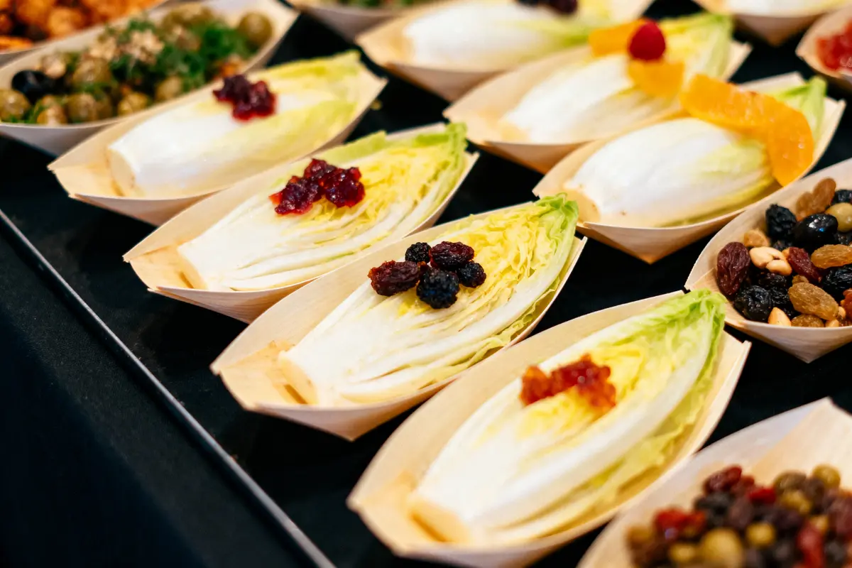 Assortiment de feuilles d'endive garnies de fruits secs, présentées dans des plats en bois sur un fond sombre.