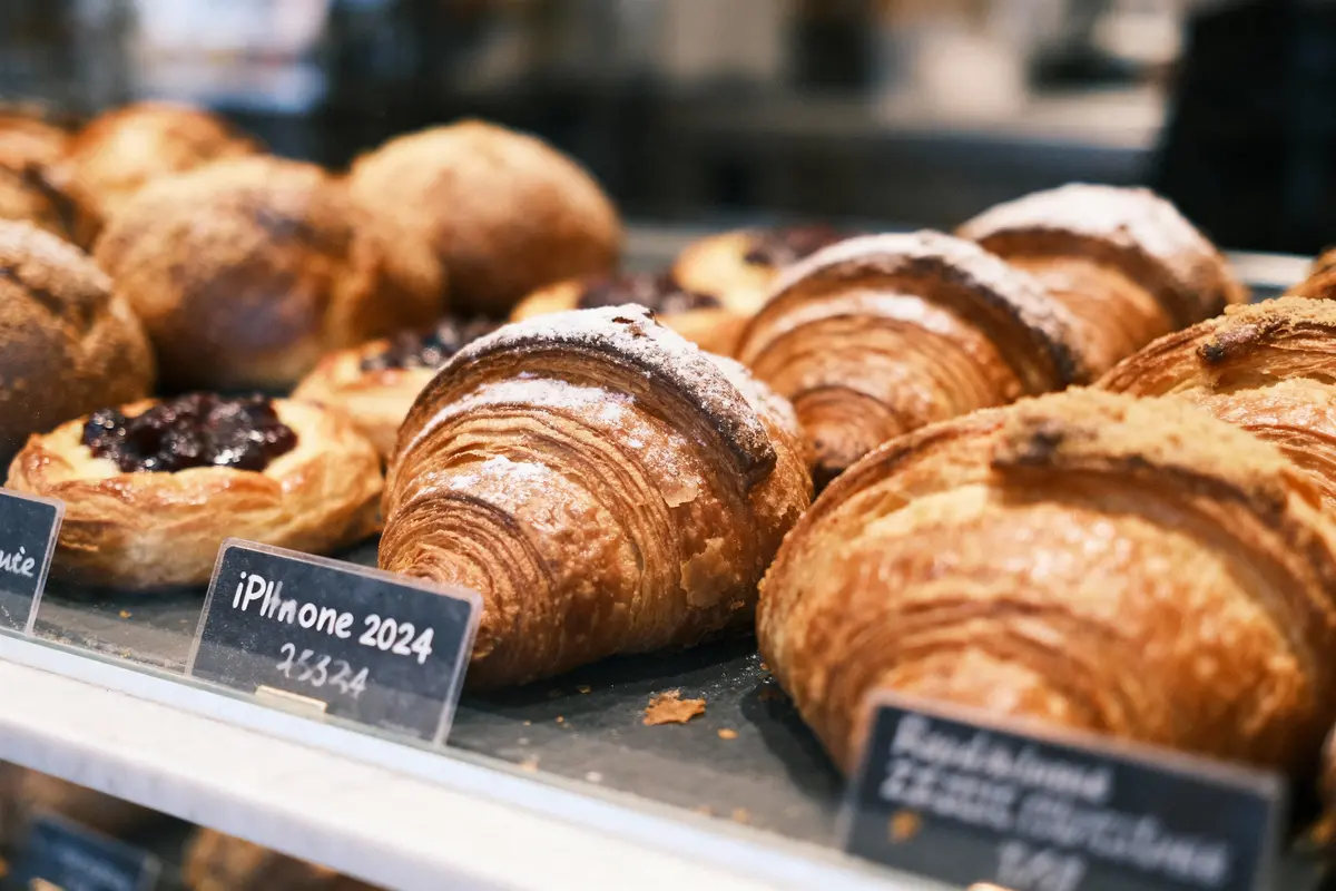 Vitrine de pâtisserie avec des croissants dorés et feuilletés, accompagnés de tartes aux fruits. Étiquettes en gros plan.
