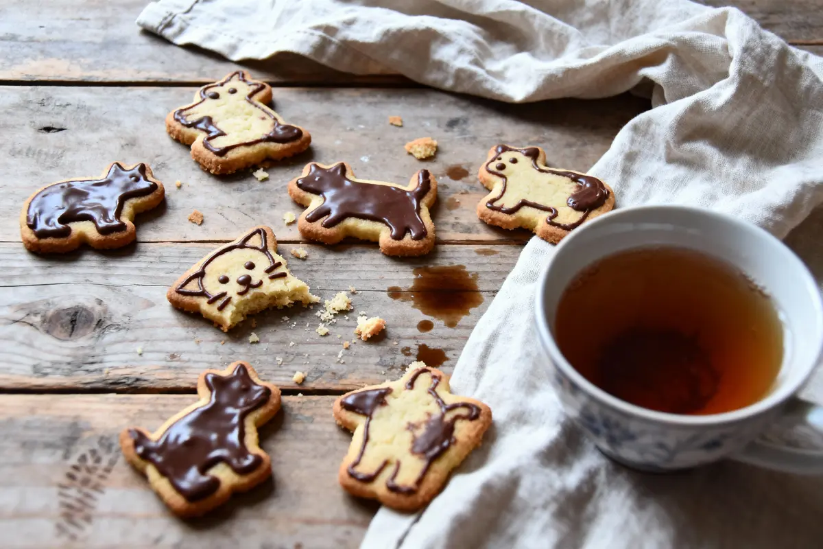 Des biscuits en forme de chats et chiens, avec du chocolat, disposés sur une table en bois à côté d'une tasse de thé.