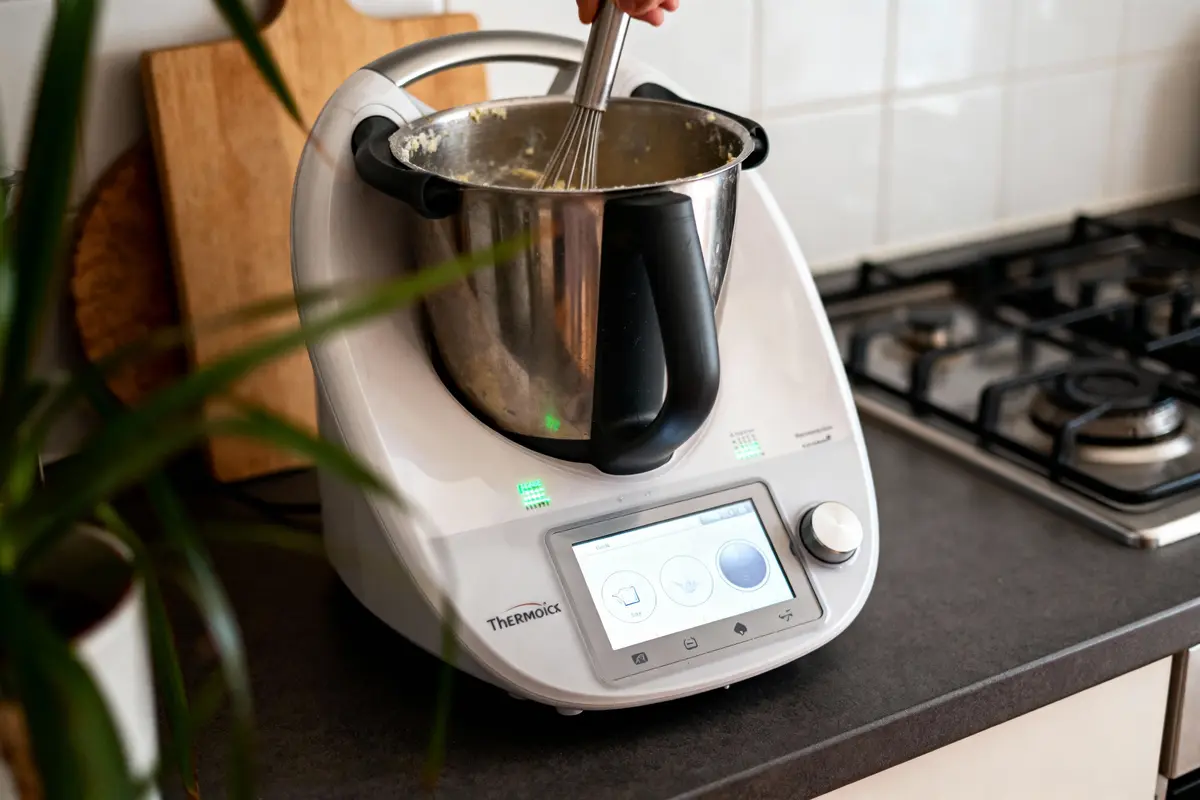 Robot culinaire Thermomix en cuisine, mélangeant des ingrédients dans un bol en acier inoxydable.