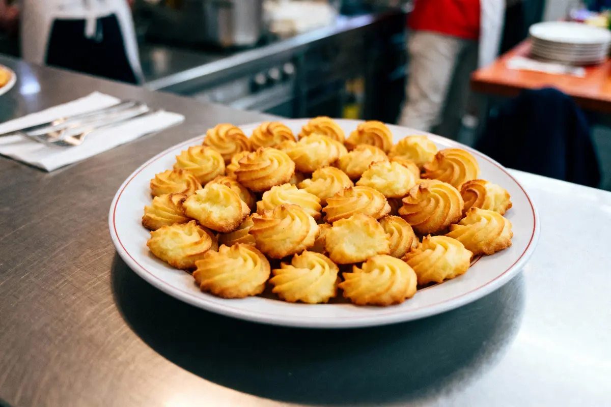 Assiette de pommes duchesse dorées servie dans une cuisine, fourchettes sur serviette à côté.