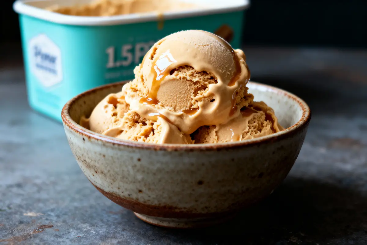 Bol de crème glacée caramel, pot en arrière-plan flou, sur surface sombre.