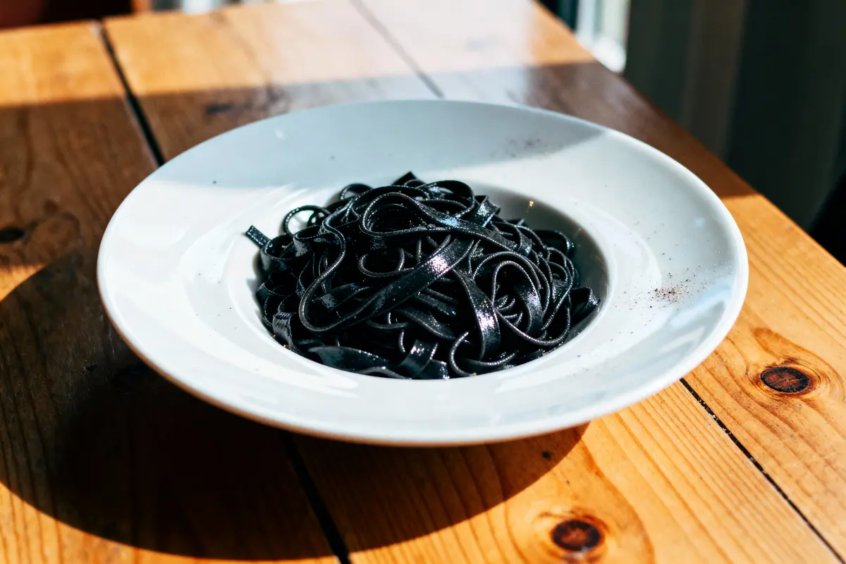 Assiette de tagliatelles noires au charbon, posée sur une table en bois, éclairée par la lumière naturelle.