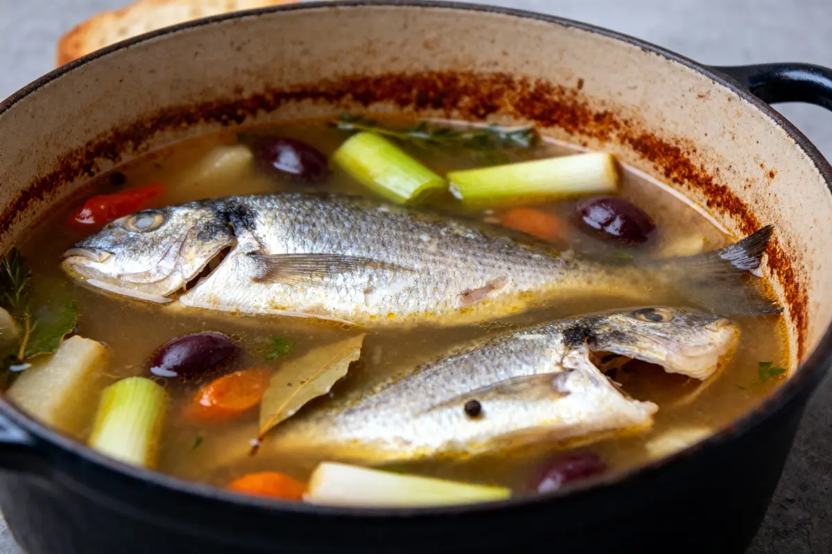 Soupe de poisson avec légumes, olives et feuilles de laurier dans une casserole en fonte.