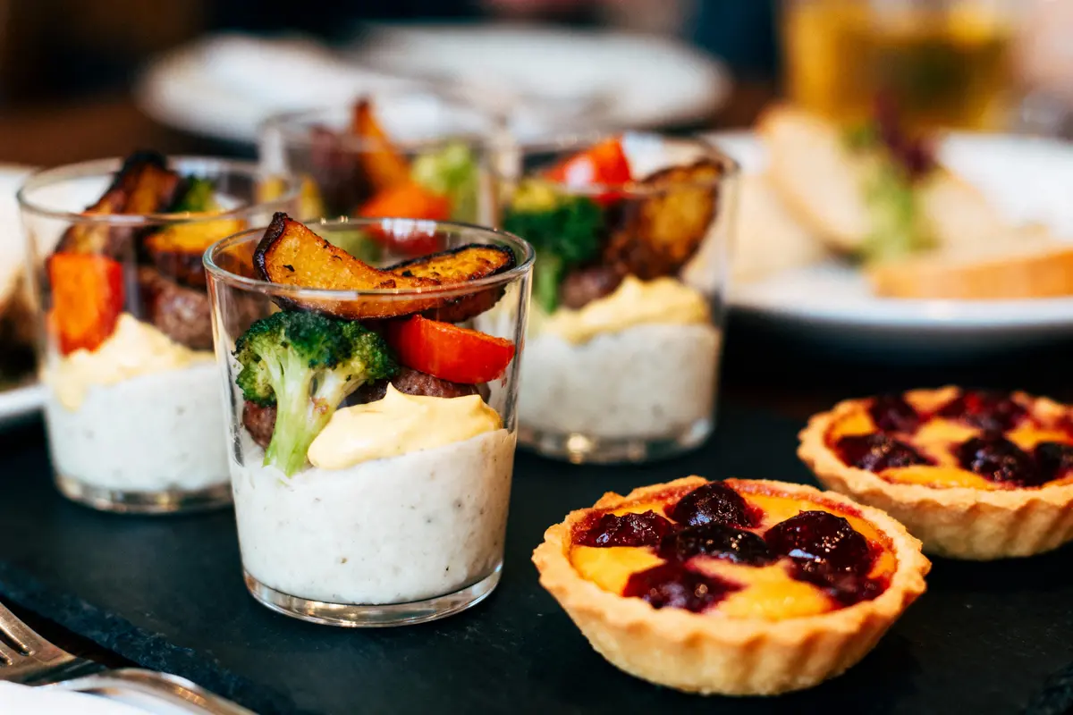 Assiettes de verrines salées avec légumes, purée et tartelettes fruits rouges, sur ardoise noire.