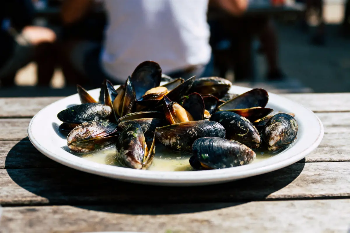 Assiette de moules cuites servie en plein air sur une table en bois, arrière-plan flou.