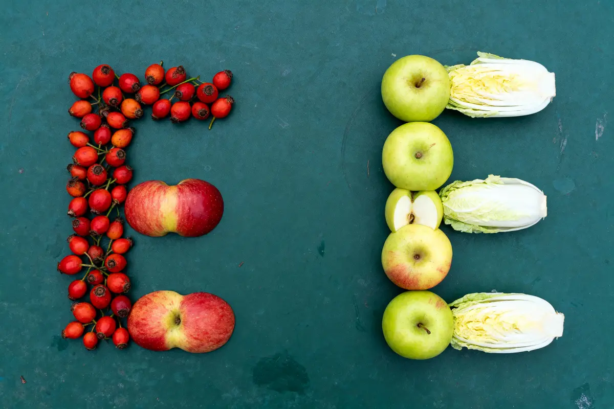 Lettres "E" formées avec fruits rouges et verts, laitues entières, sur fond vert.