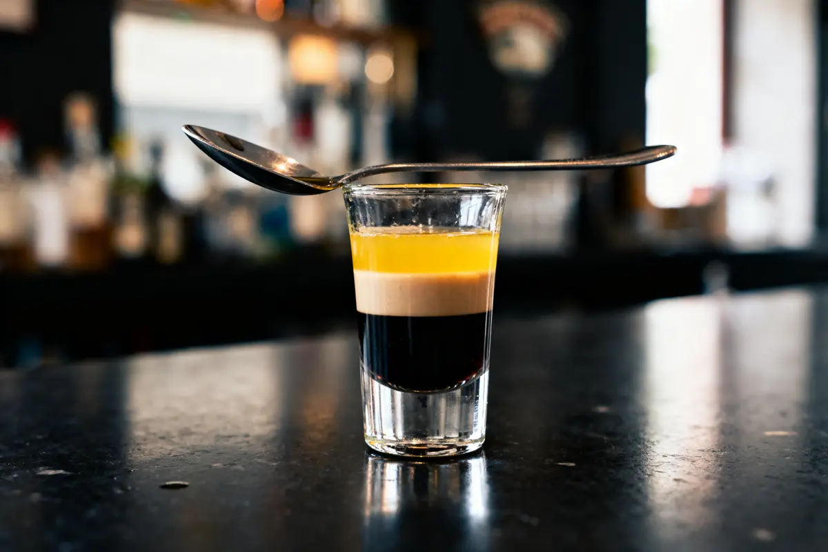 Verre de shooter à trois couches avec cuillère posée dessus, sur un comptoir de bar.