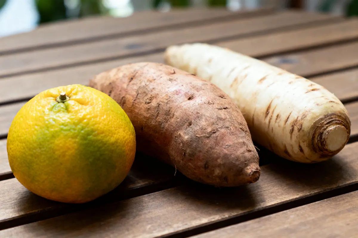 Orange, patate douce, et panais posés sur une table en bois. Légumes et fruit frais à l'extérieur.