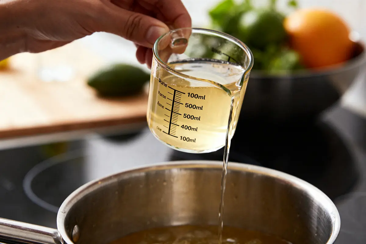 Main versant 100 ml en cl de liquide d'une tasse graduée dans une casserole