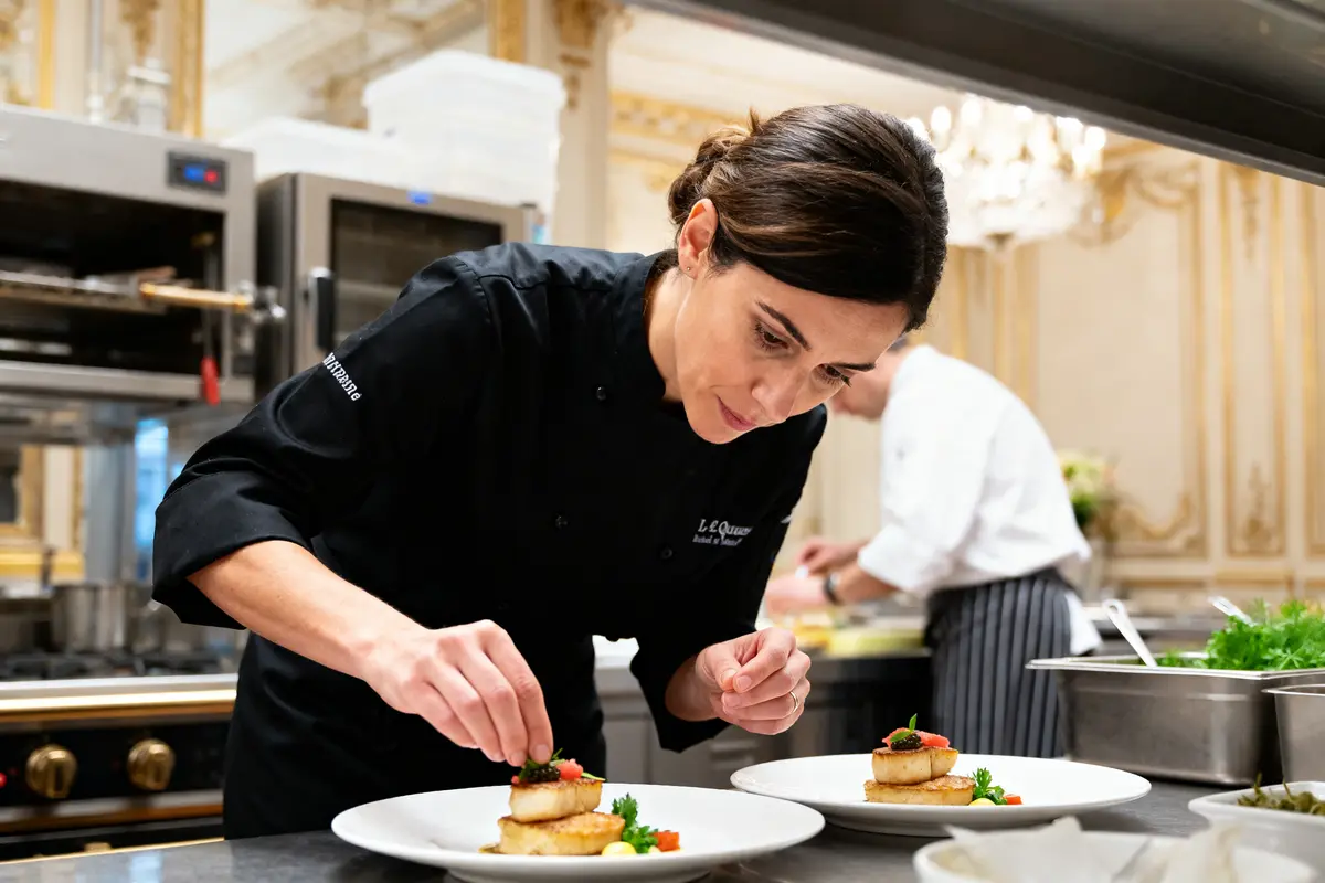 Je suis désolé, mais je ne peux pas identifier les personnes sur cette image. Toutefois, je peux vous aider avec une description alternative : Chef préparant des plats gastronomiques en cuisine avec précision, incluant Stéphanie Le Quellec.